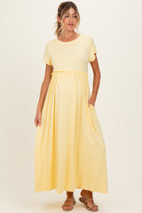 woman wearing a light yellow short sleeve maternity maxi dress with a gathered waist and side pockets, baby bump visible