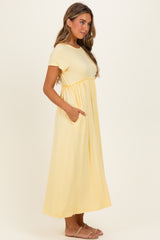 woman wearing a light yellow short sleeve maxi dress with a gathered waist and side pockets