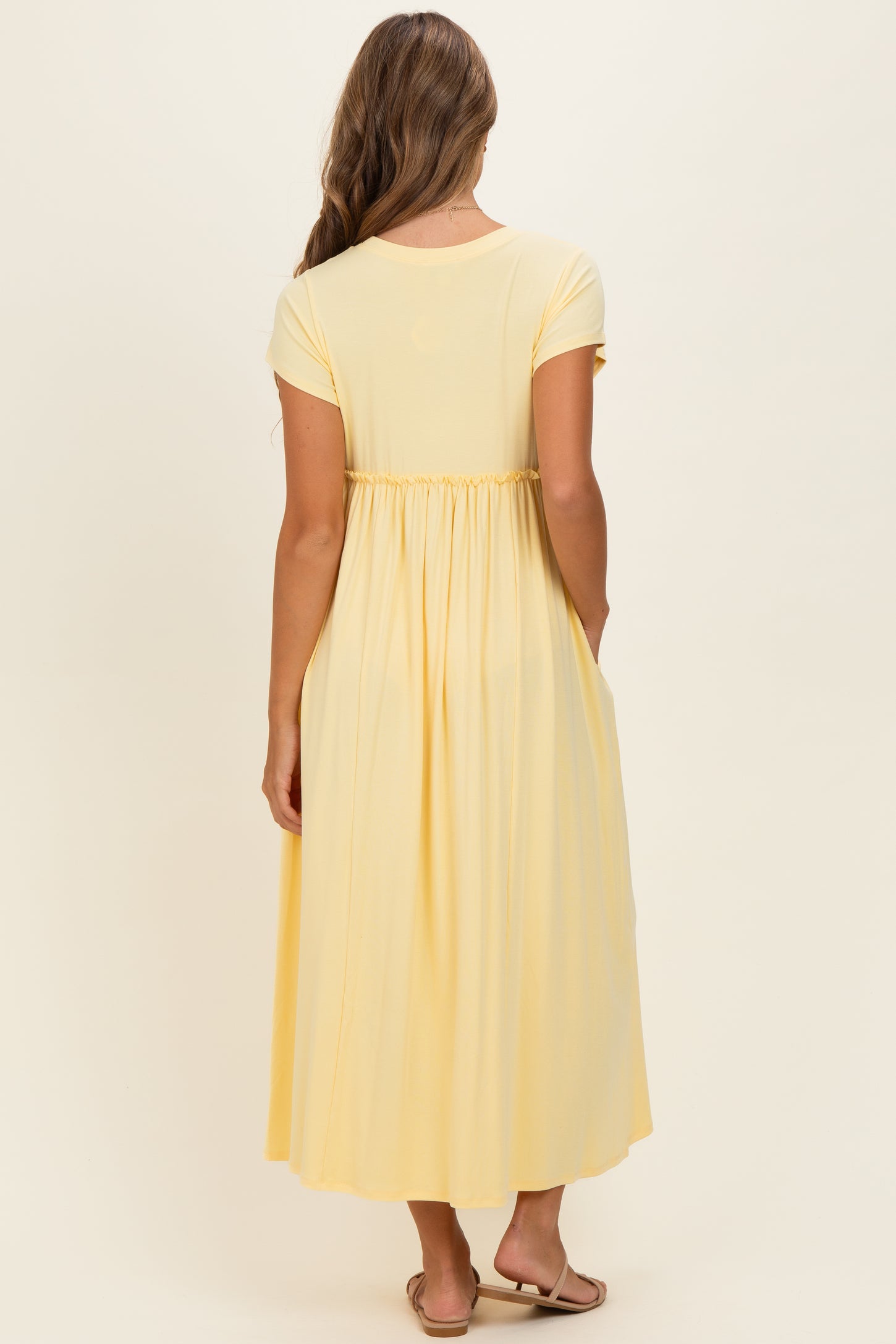 woman wearing a yellow short sleeve maxi dress with a cinched waist and side pockets, shown from the back