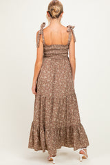 woman wearing a brown floral maternity maxi dress with tie shoulder straps, styled with a ruffled hem