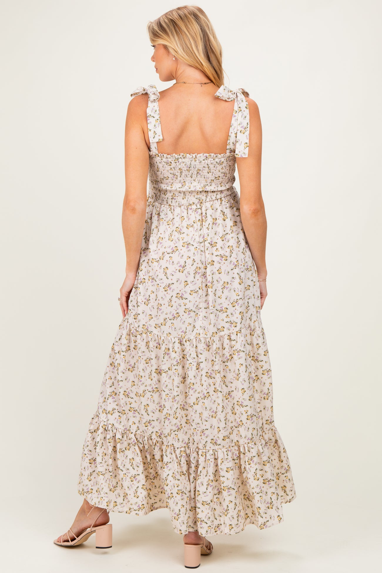 woman wearing a floral maxi maternity dress with tie straps and a tiered ruffled hem, showing a baby bump