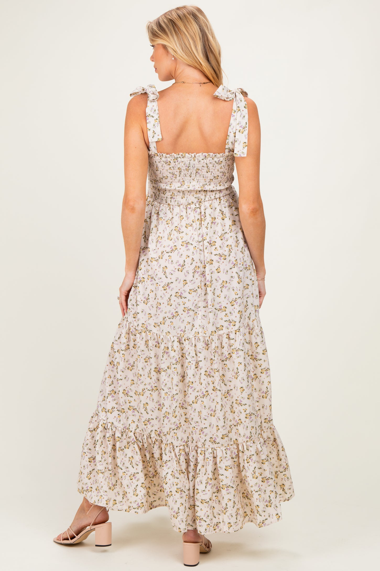 woman wearing a floral maxi maternity dress with tie straps and a tiered ruffled hem, showing a baby bump