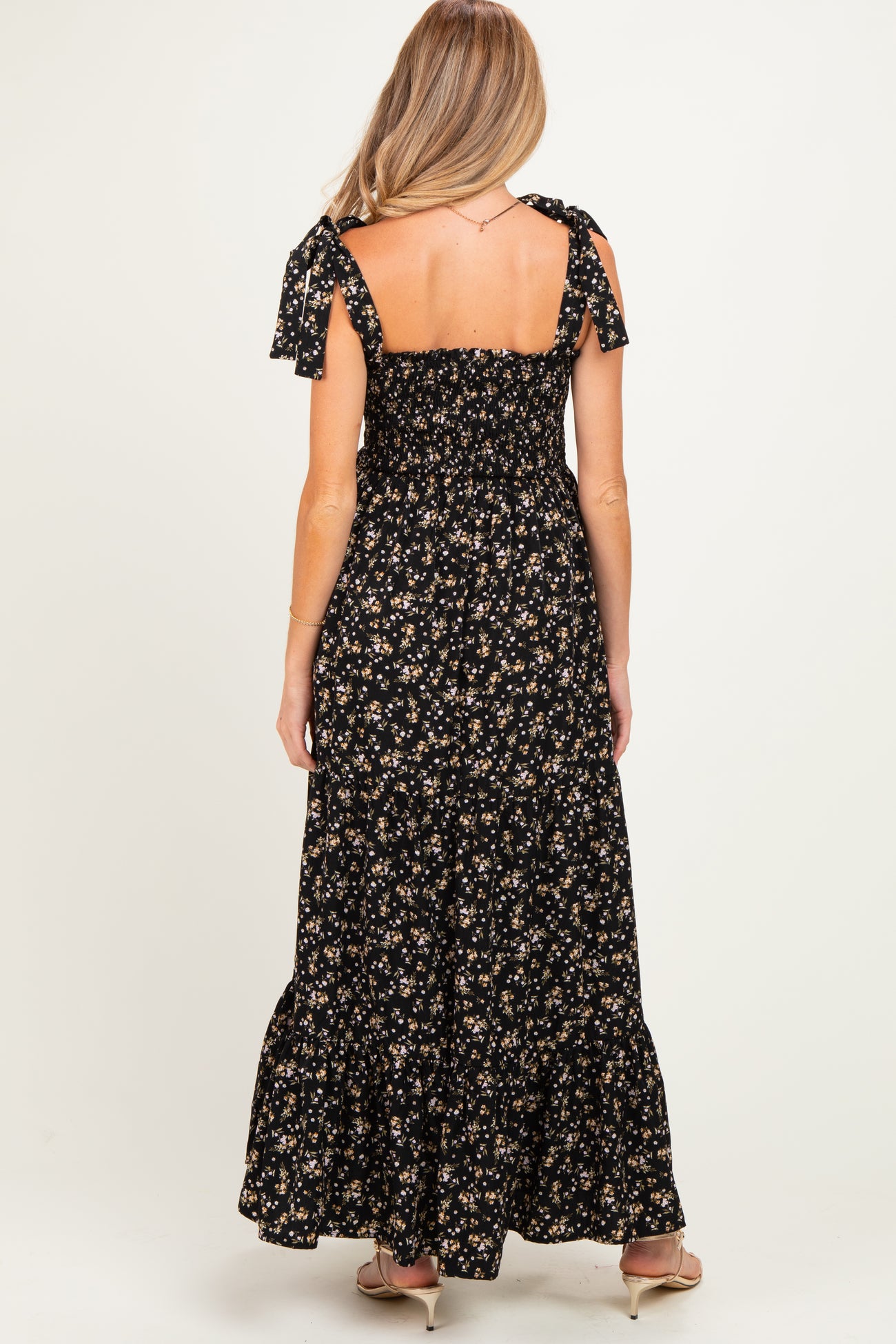 woman wearing a floral black maternity maxi dress with tie straps and a flowing skirt, showing a baby bump
