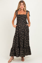 woman wearing a black floral maternity maxi dress with square neckline and tie straps, featuring pockets and a flowing silhouette