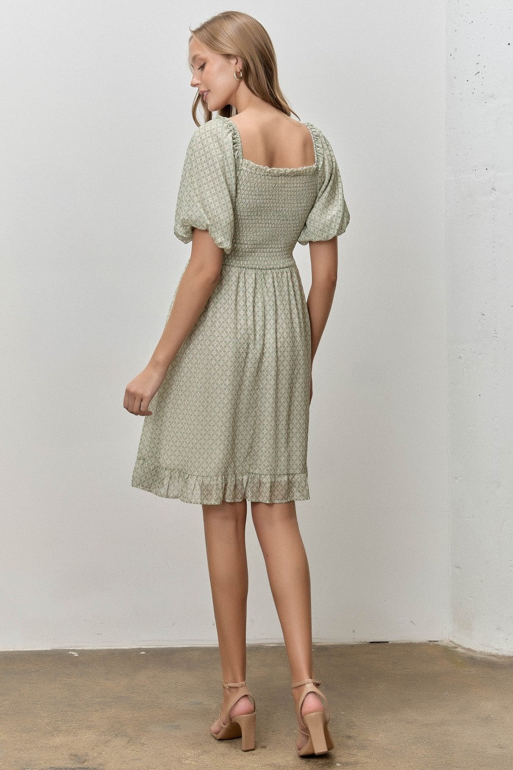 woman wearing a light green floral print dress with puff sleeves and a ruffled hem, seen from the back