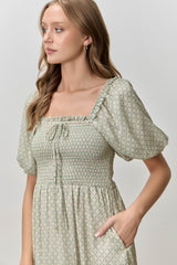 woman wearing a green floral smocked dress with puff sleeves and a square neckline, featuring side pockets