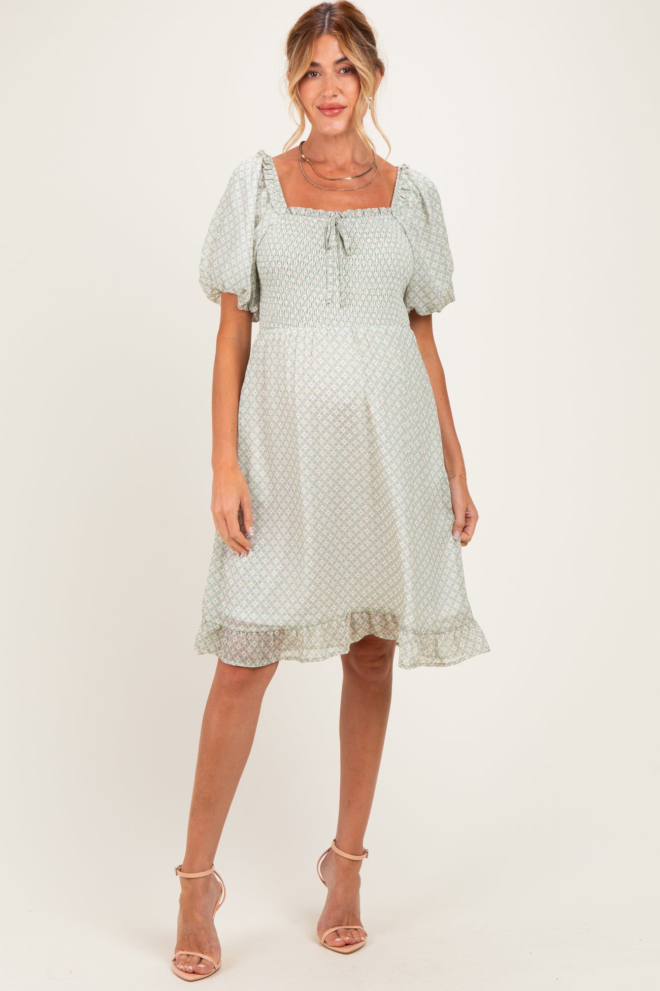 woman wearing a light green maternity dress with puff sleeves and a square neckline, standing and showcasing her baby bump