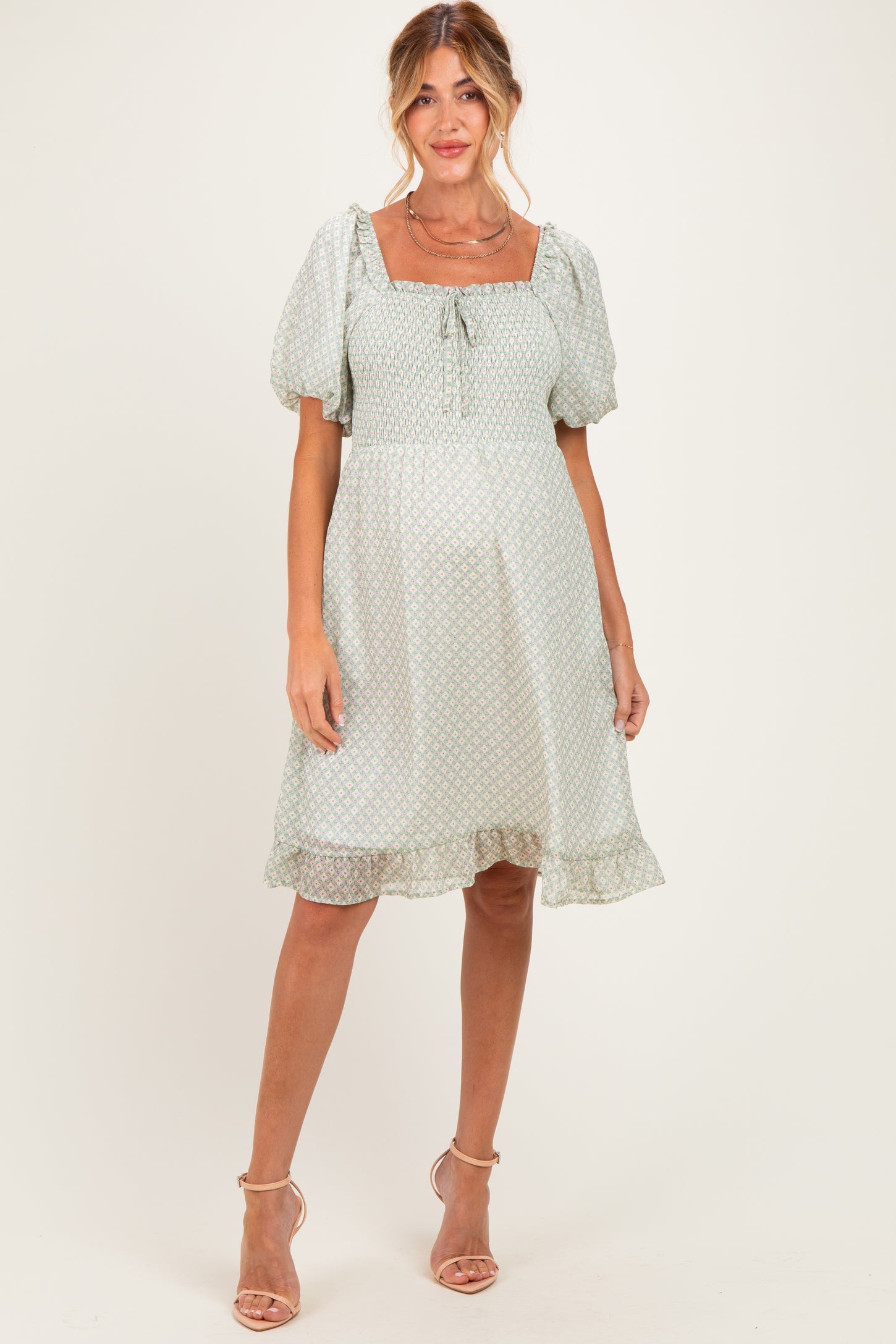 woman wearing a light green maternity dress with puff sleeves and a square neckline, standing and showcasing her baby bump