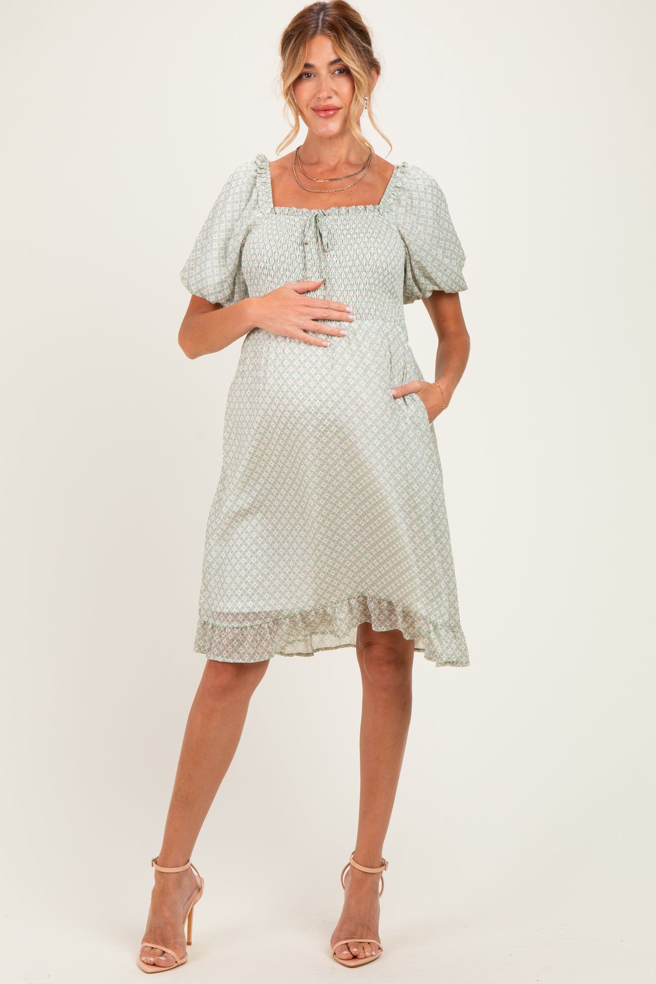 woman wearing a mint green floral print maternity dress with puff sleeves and a tied neckline, showing her baby bump