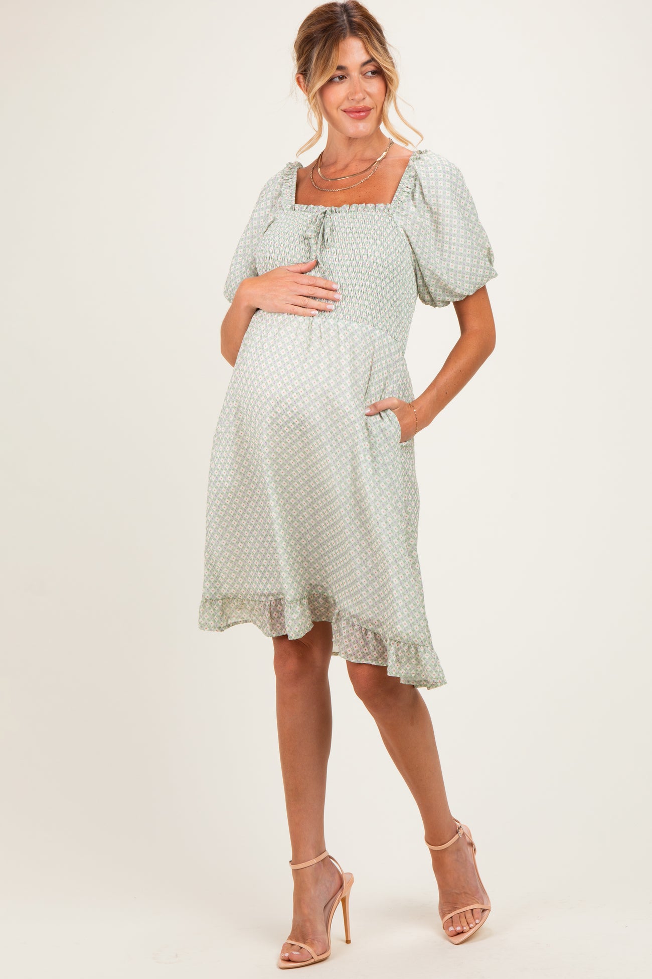 woman wearing a light green short sleeve maternity dress with a square neckline and ruffled hem, holding her baby bump