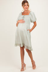 woman wearing a light green short sleeve maternity dress with a square neckline and ruffled hem, holding her baby bump