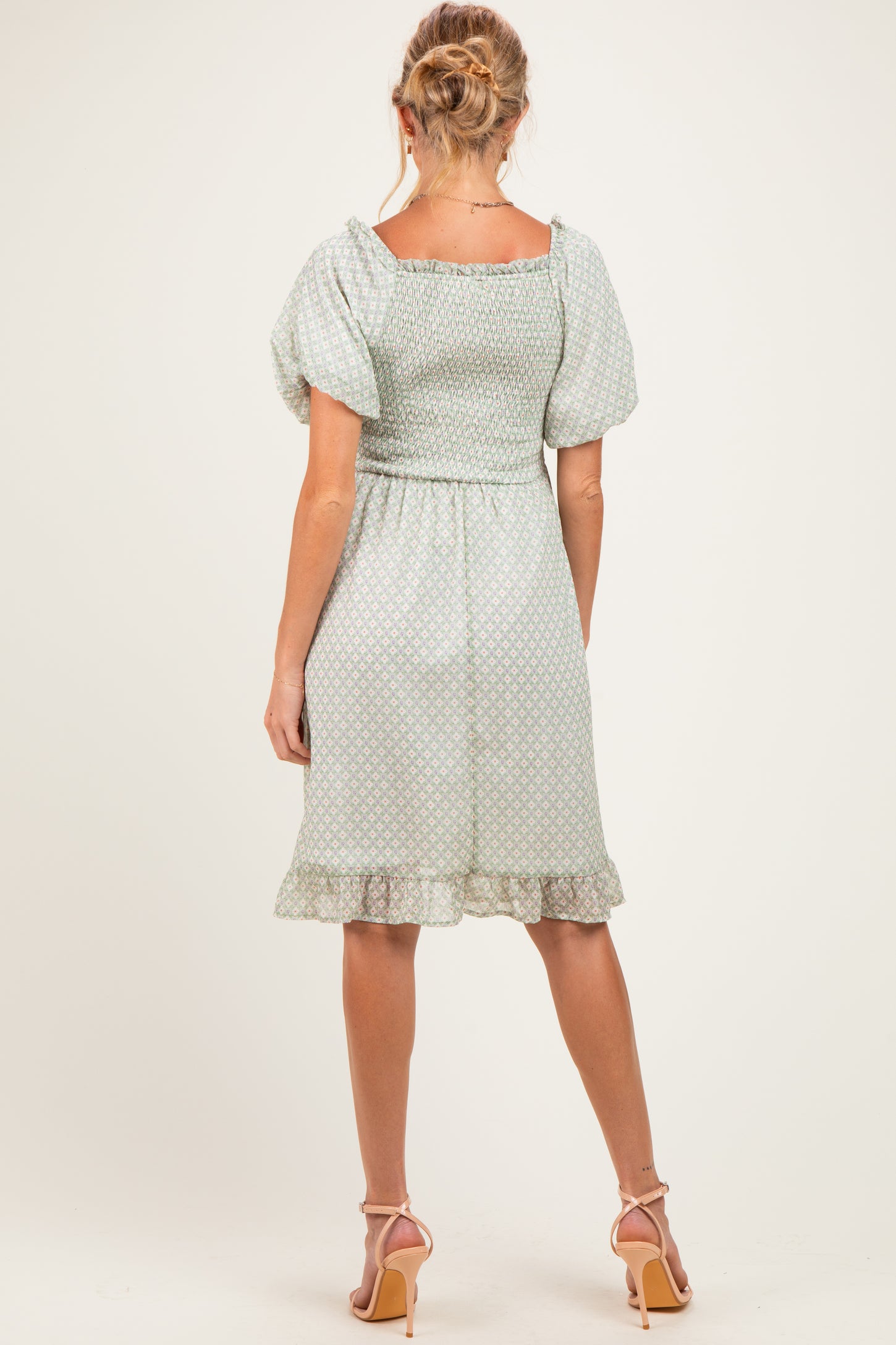 woman wearing a mint green maternity dress with puff sleeves and a ruffled hem, showing off her baby bump