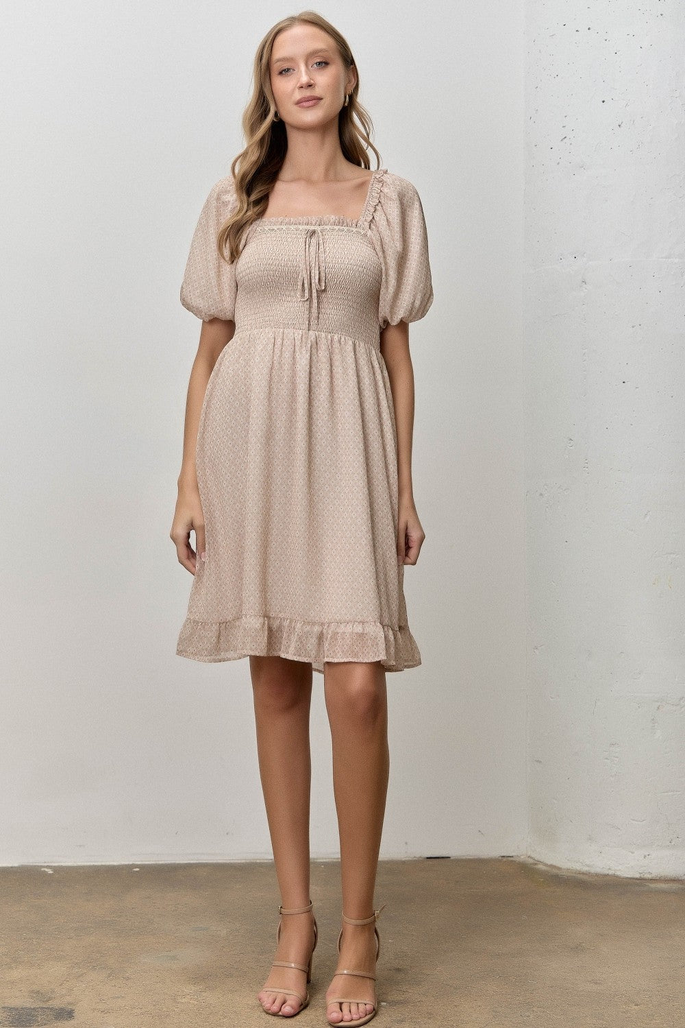 woman wearing a beige puff sleeve smocked dress with a square neckline and ruffle hem