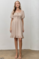 woman wearing a beige puff sleeve smocked dress with a square neckline and ruffle hem
