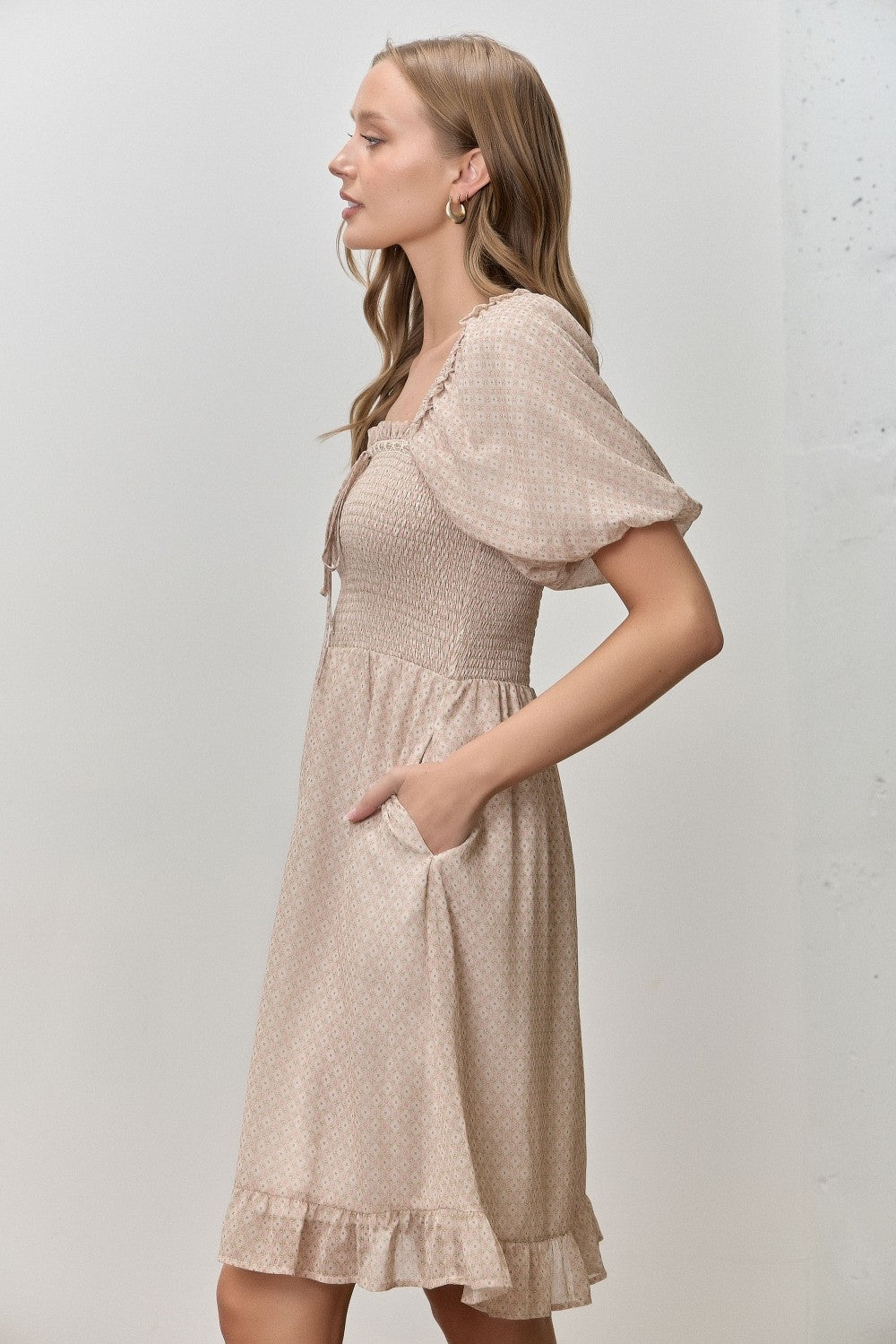 woman wearing a beige short sleeve dress with smocked bodice, puffed sleeves, and pockets