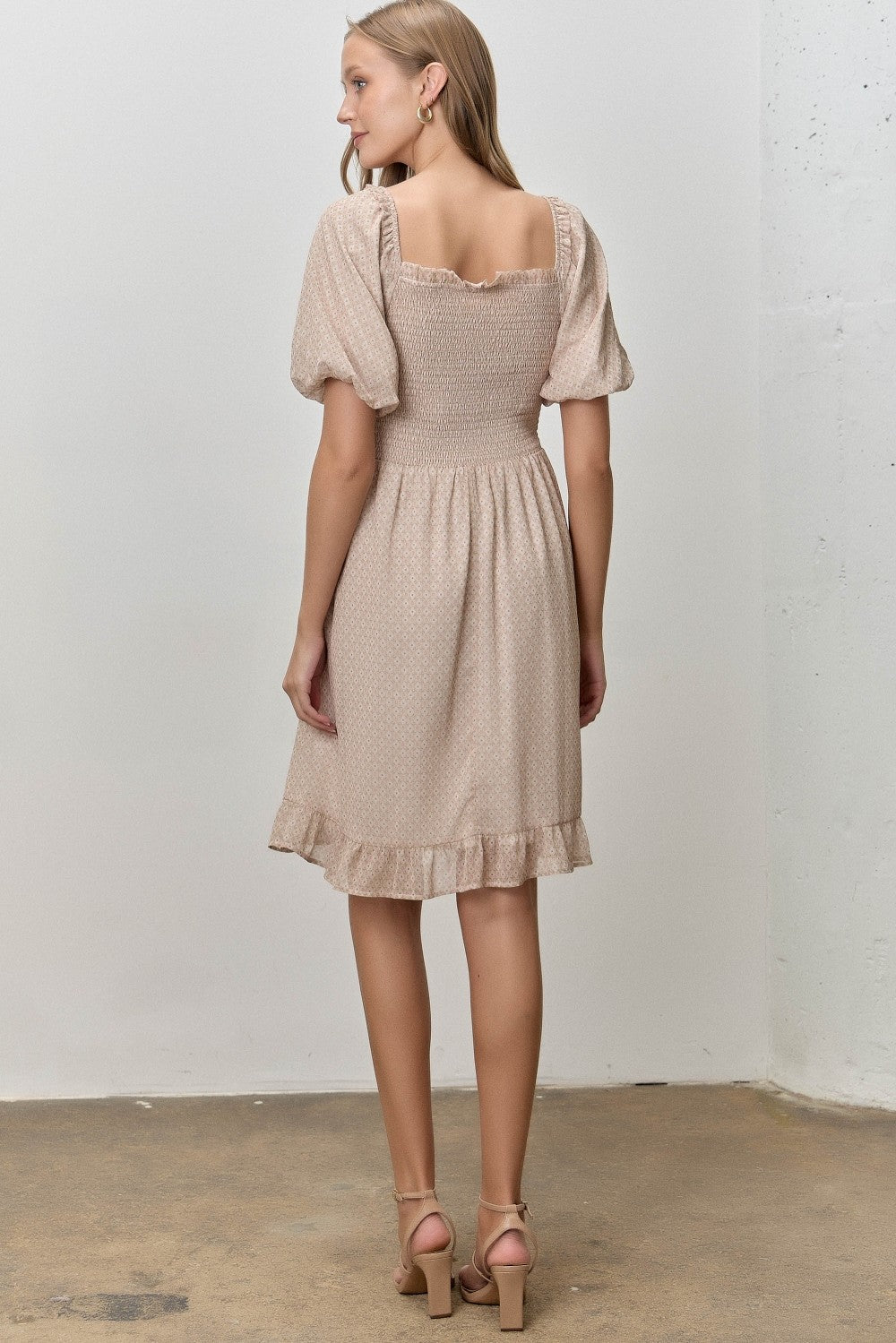 woman wearing a beige short sleeve dress with a smocked bodice and ruffled hem, viewed from the back