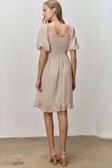 woman wearing a beige short sleeve dress with a smocked bodice and ruffled hem, viewed from the back