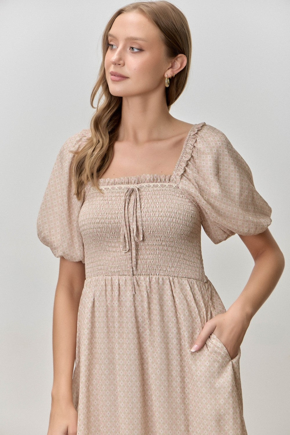 woman wearing a beige square neck dress with puff sleeves and a smocked bodice, featuring pockets