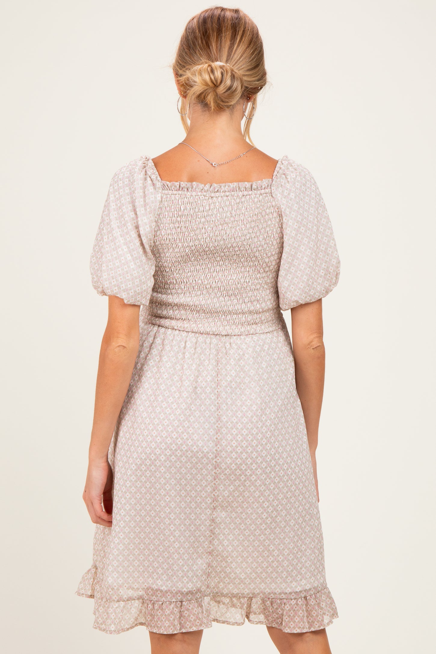 woman wearing a maternity off-white puff sleeve dress with a smocked bodice and ruffled hem, showing her back