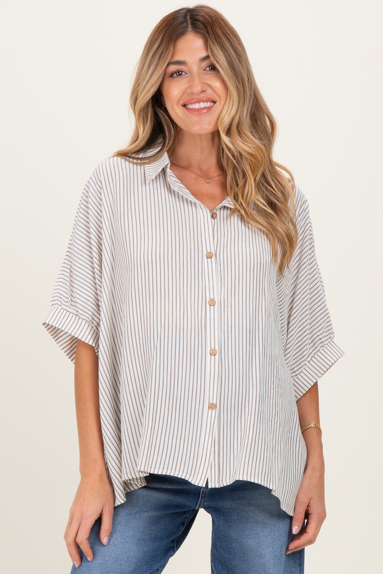 woman wearing a beige and white striped maternity shirt with short sleeves and buttons, paired with blue jeans