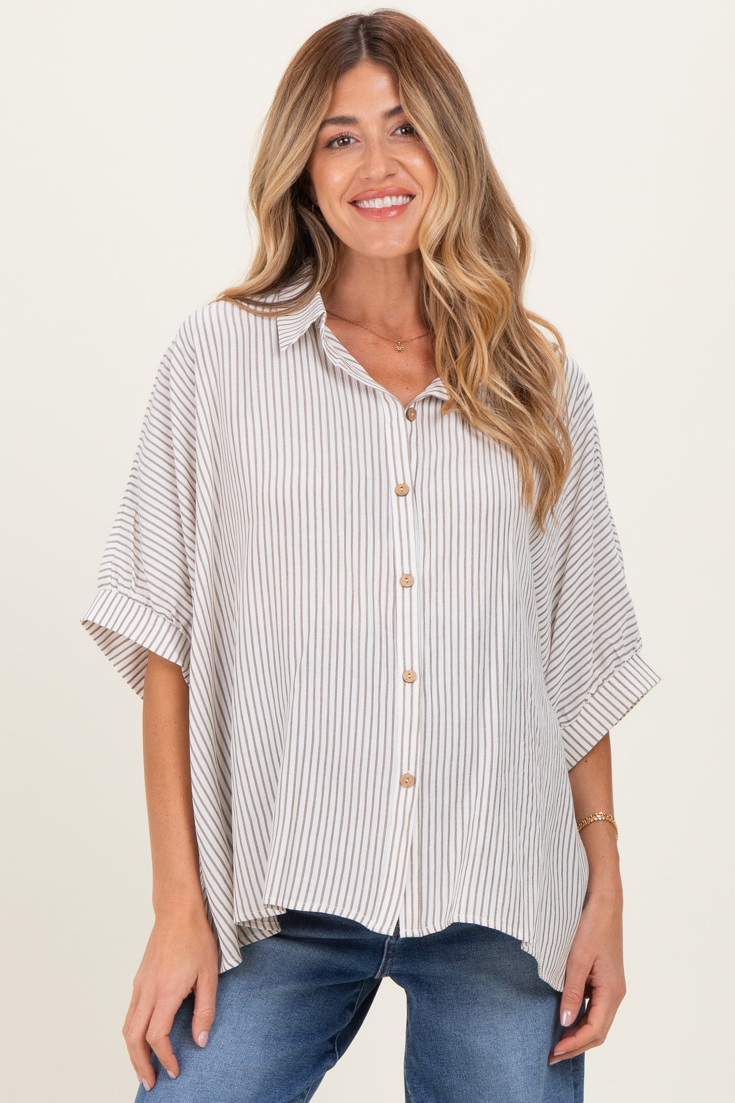 woman wearing a beige and white striped maternity shirt with short sleeves and buttons, paired with blue jeans