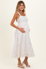 woman wearing a white floral midi maternity dress and holding her baby bump
