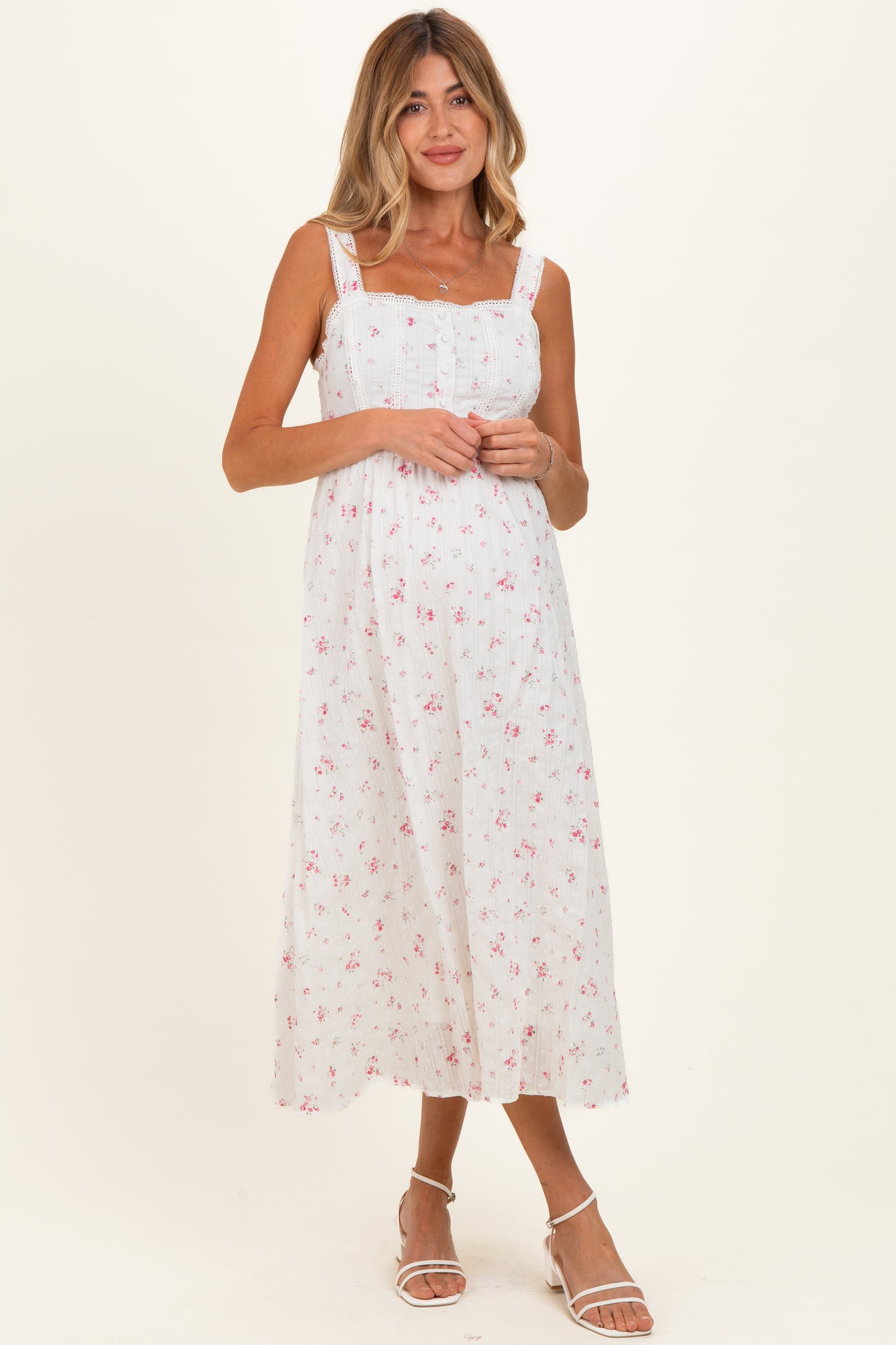woman wearing a white floral maternity dress with adjustable straps and a cinched bodice, showing her baby bump