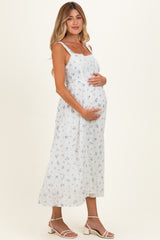 woman wearing a white floral maternity dress and holding her baby bump