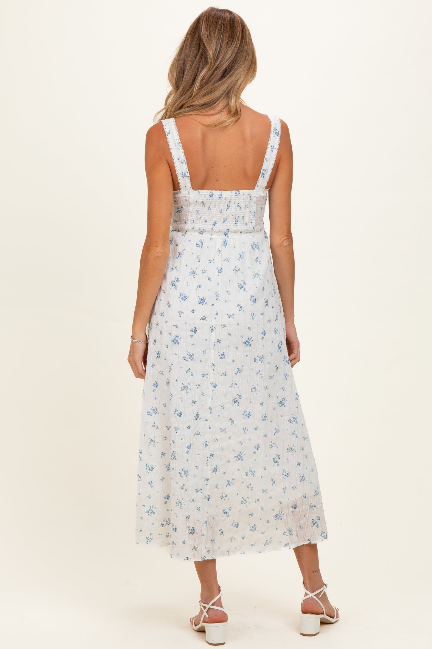 woman wearing a white maternity dress with blue floral prints and adjustable straps, showing the back view