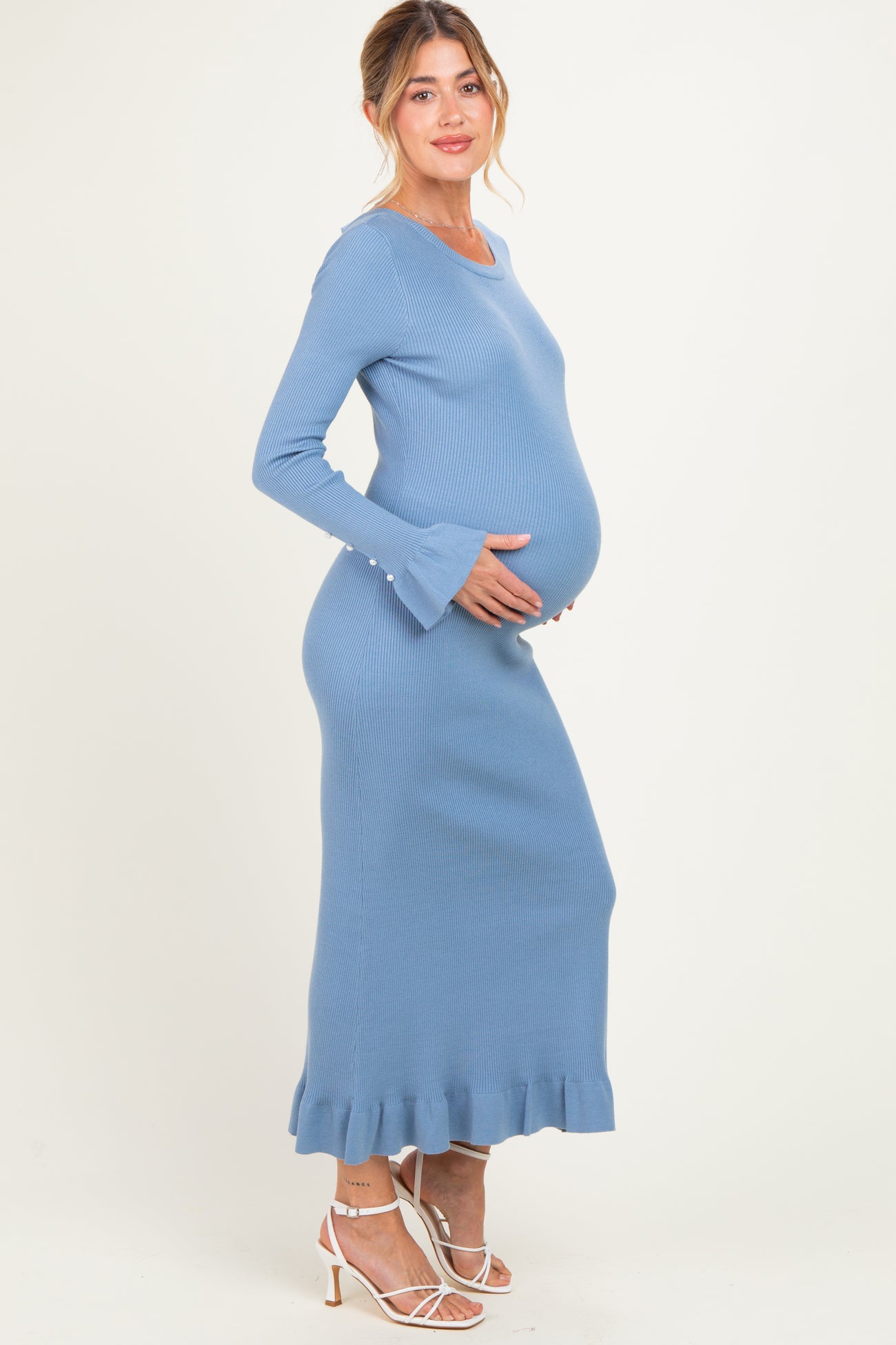 woman wearing a light blue maternity ribbed maxi dress with flared sleeves and ruffle hem, showing her baby bump