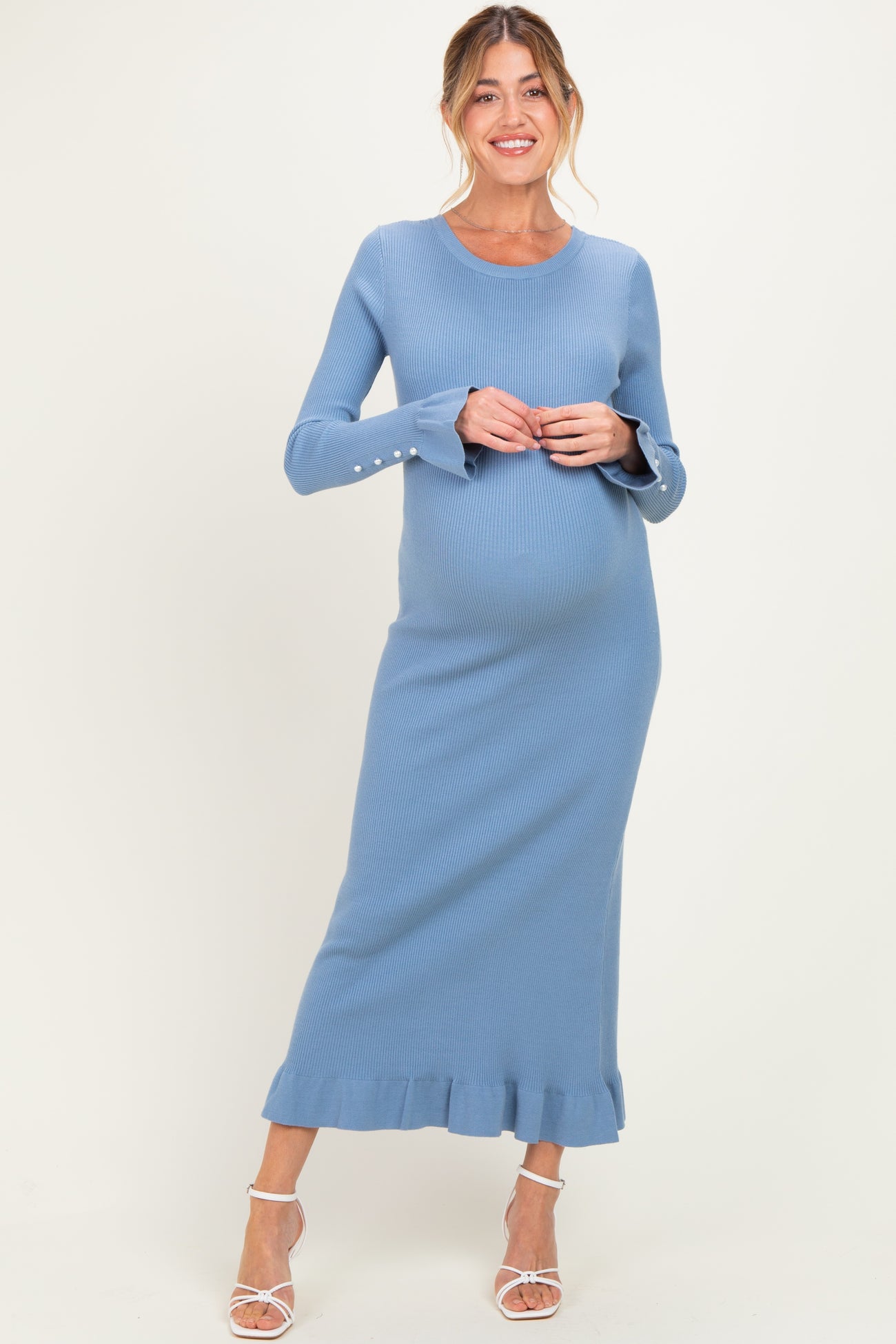 woman wearing a light blue ribbed maternity dress with long sleeves and ruffle hem, showing her baby bump