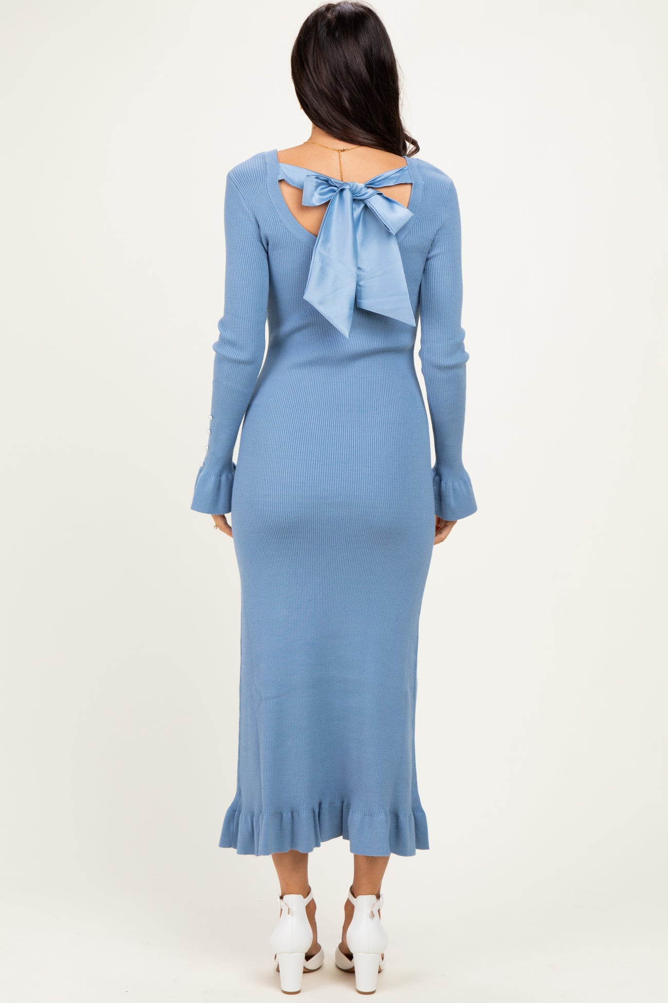 woman wearing a light blue ribbed midi dress with a bow detail at the back and ruffled hem