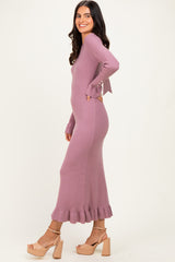 woman wearing a ribbed mauve-colored maxi dress with flared sleeves and a ruffled hem, paired with beige block-heeled sandals