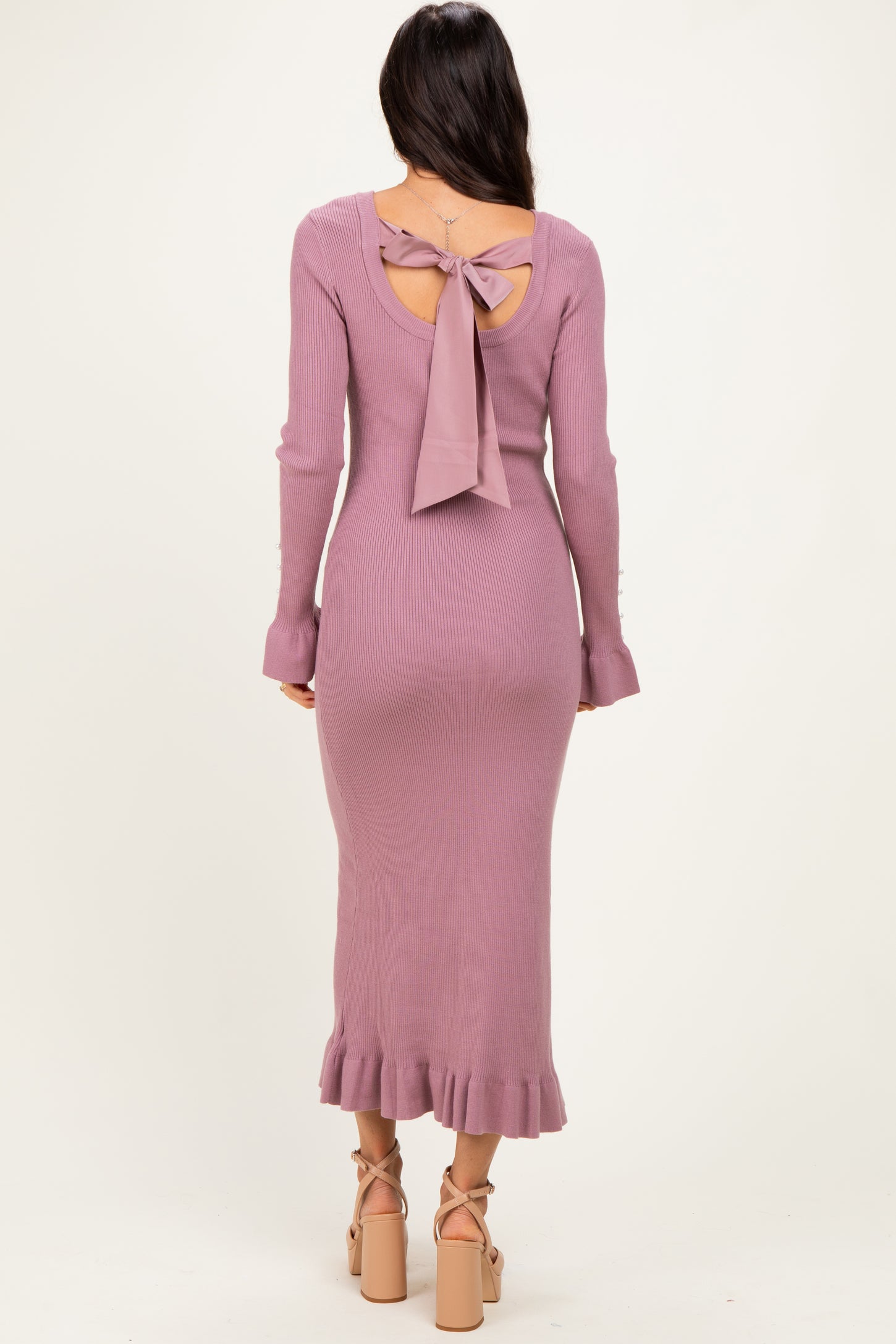 woman wearing a lavender ribbed midi dress with a tie back and ruffle hem, showcasing her back and legs