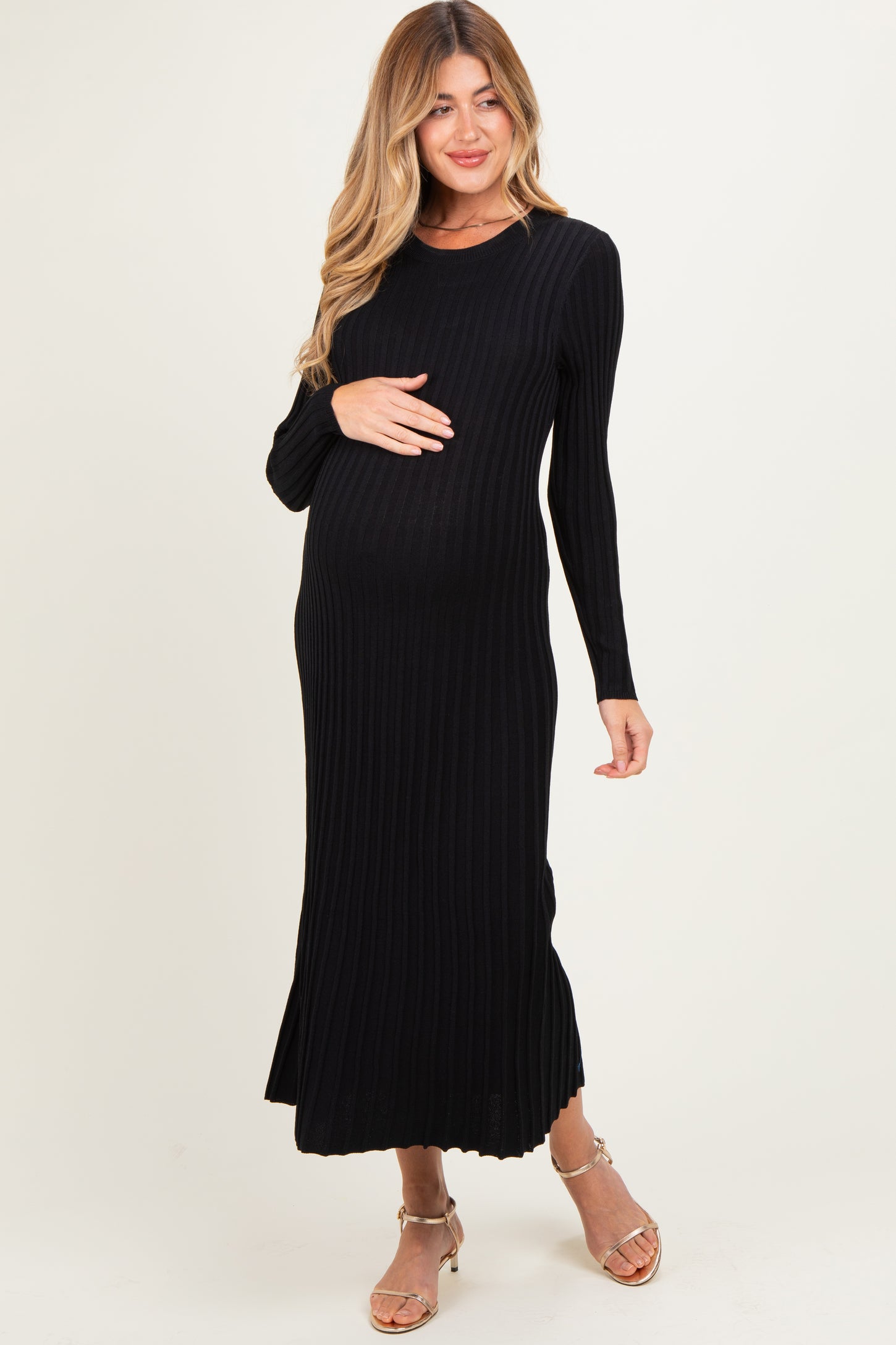 woman wearing a black ribbed maternity dress, holding her baby bump, with long sleeves and a midi length