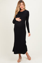 woman wearing a black ribbed maternity dress, holding her baby bump, with long sleeves and a midi length