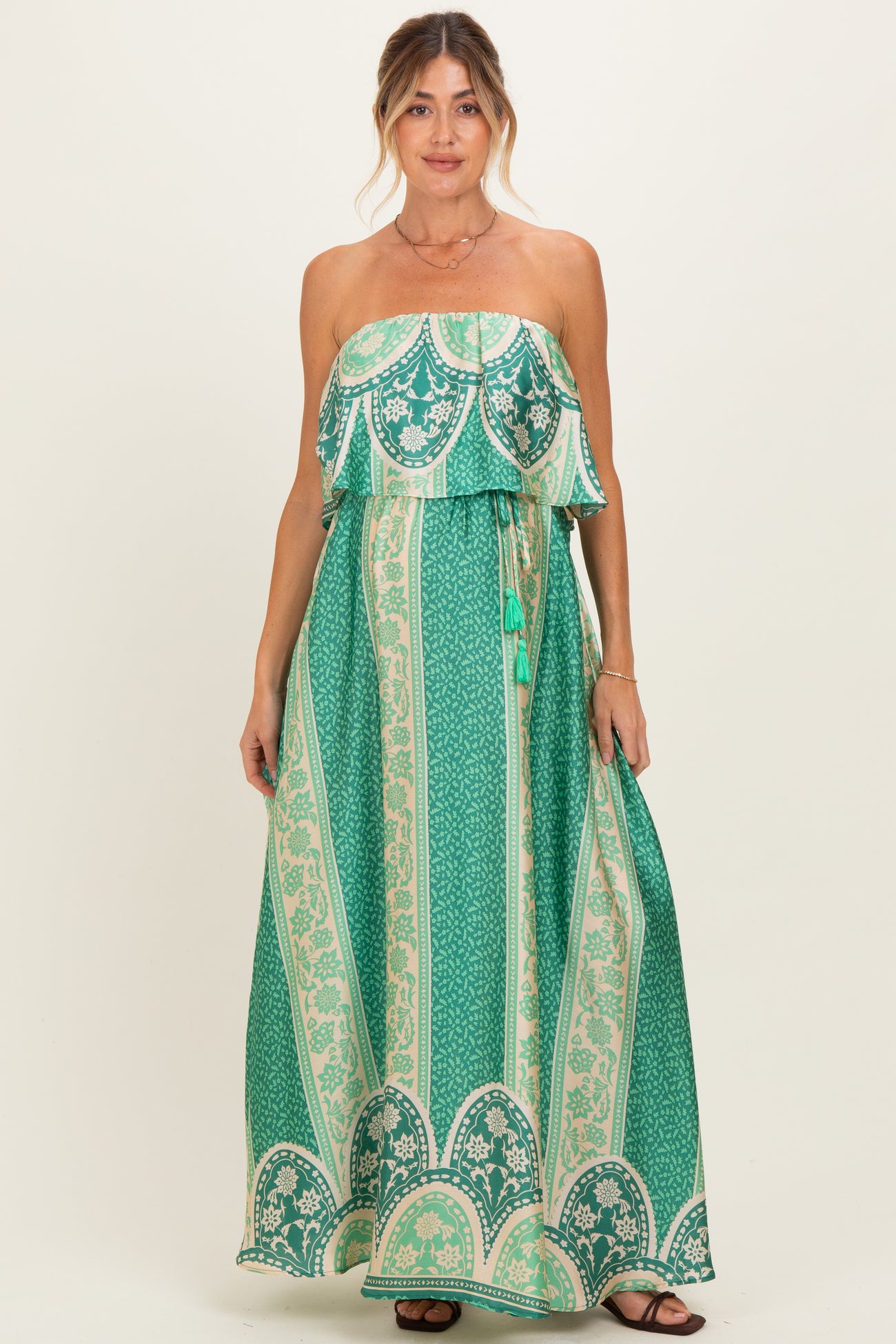 woman wearing a green strapless maxi maternity dress with a tiered design and patterned details, holding her baby bump