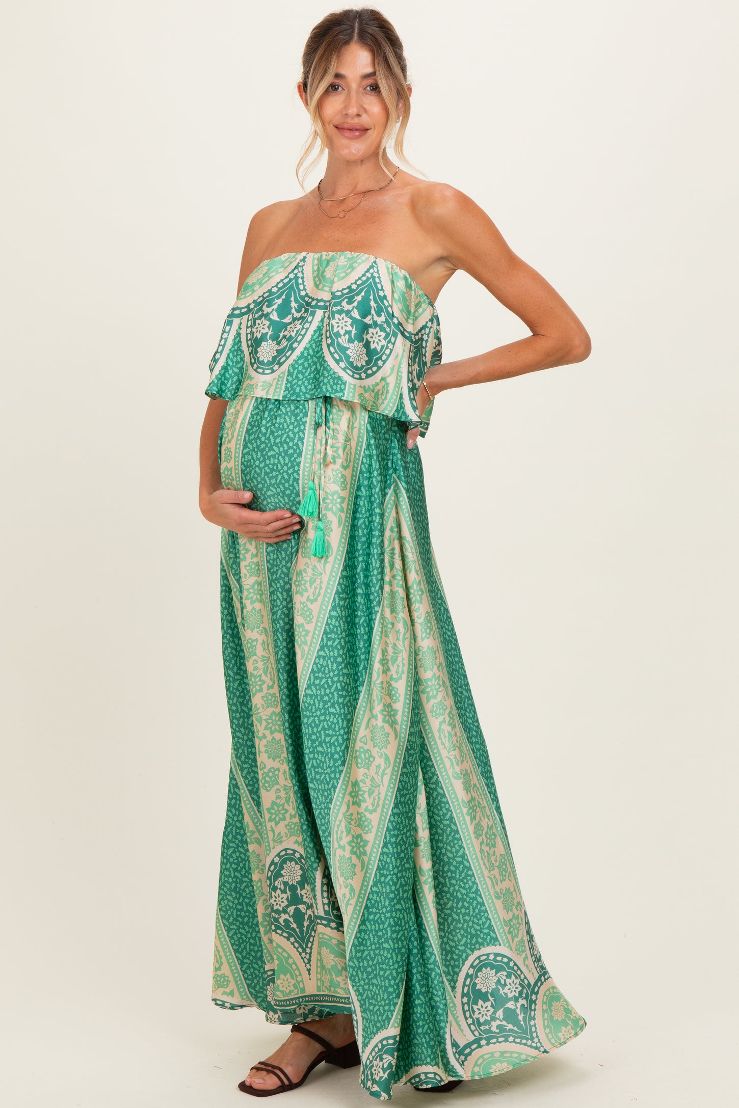 woman wearing a green printed maternity maxi dress with a ruffled off-the-shoulder style and showing her baby bump