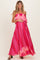 woman wearing a vibrant pink strapless maternity dress with a ruffled overlay and holding her baby bump