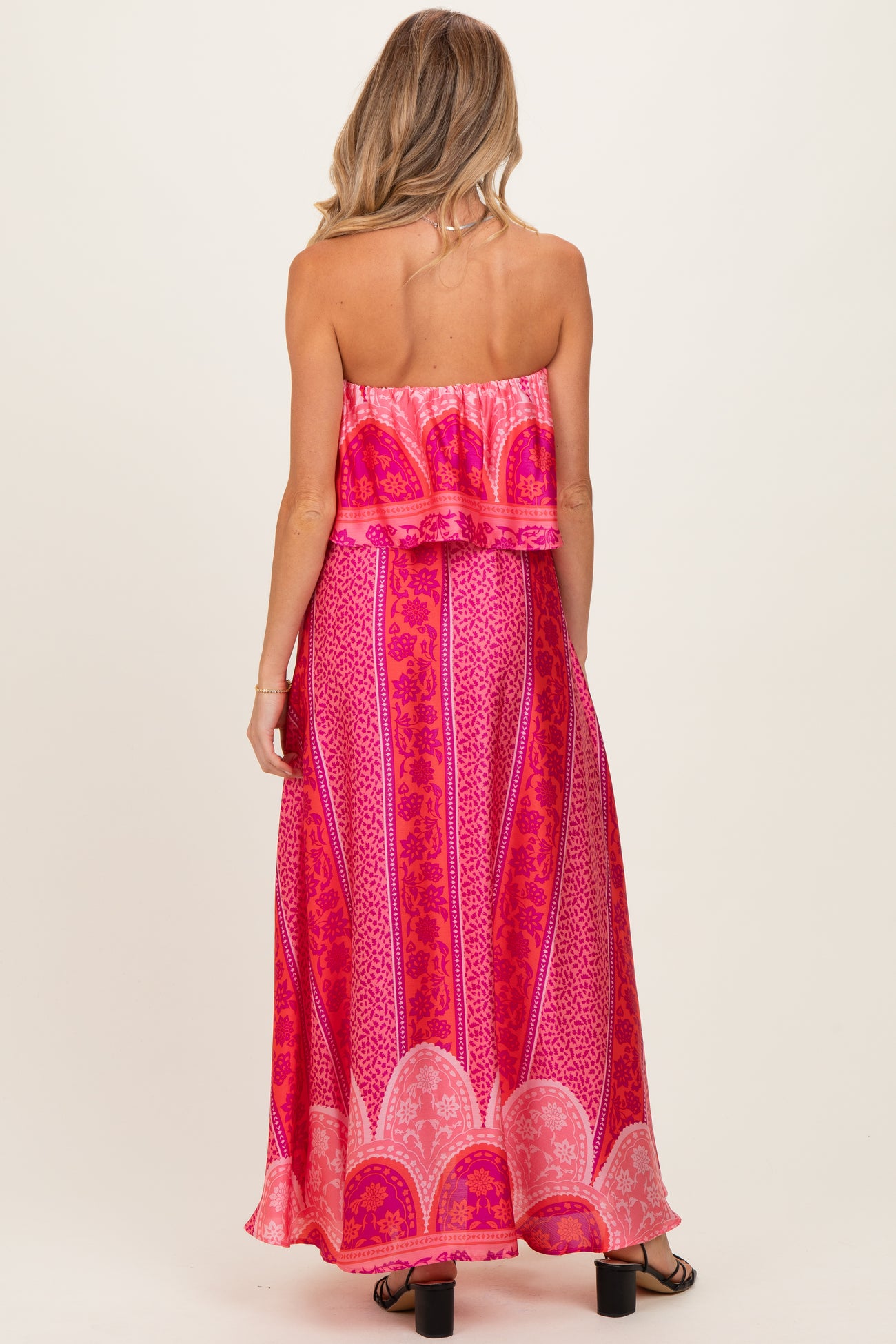 woman wearing a pink strapless maternity maxi dress with a layered ruffle detail and a vibrant patterned design