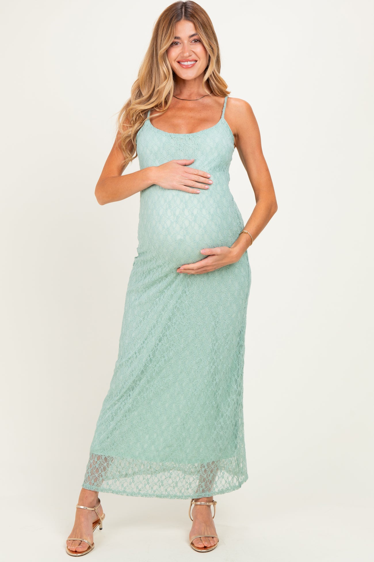 woman wearing a light green lace maternity maxi dress and gently cradling her baby bump