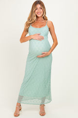 woman wearing a light green lace maternity maxi dress and gently cradling her baby bump