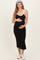 woman wearing a black maternity midi dress with white straps and holding her baby bump