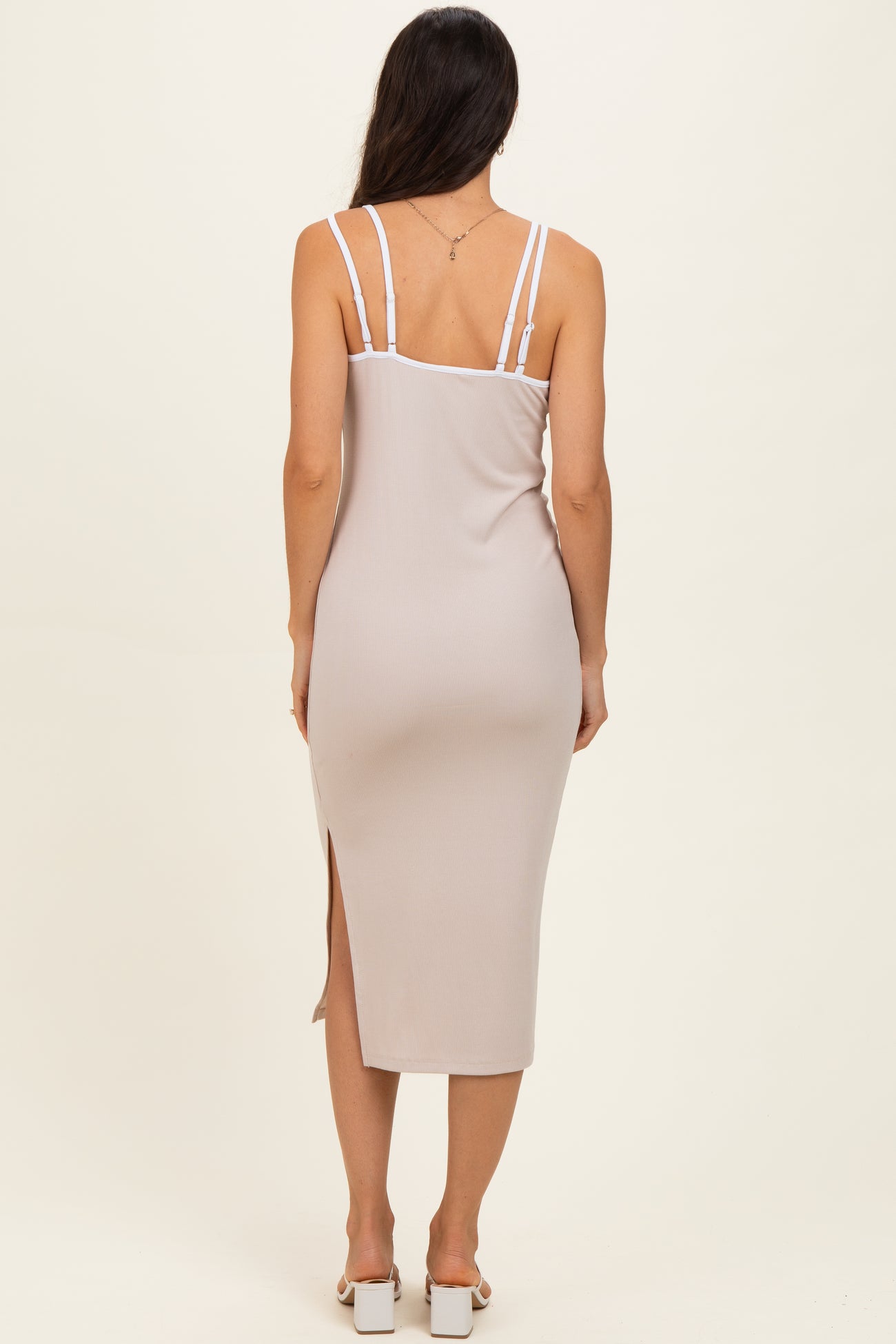 woman wearing a light beige midi dress with adjustable straps and a side slit, viewed from the back