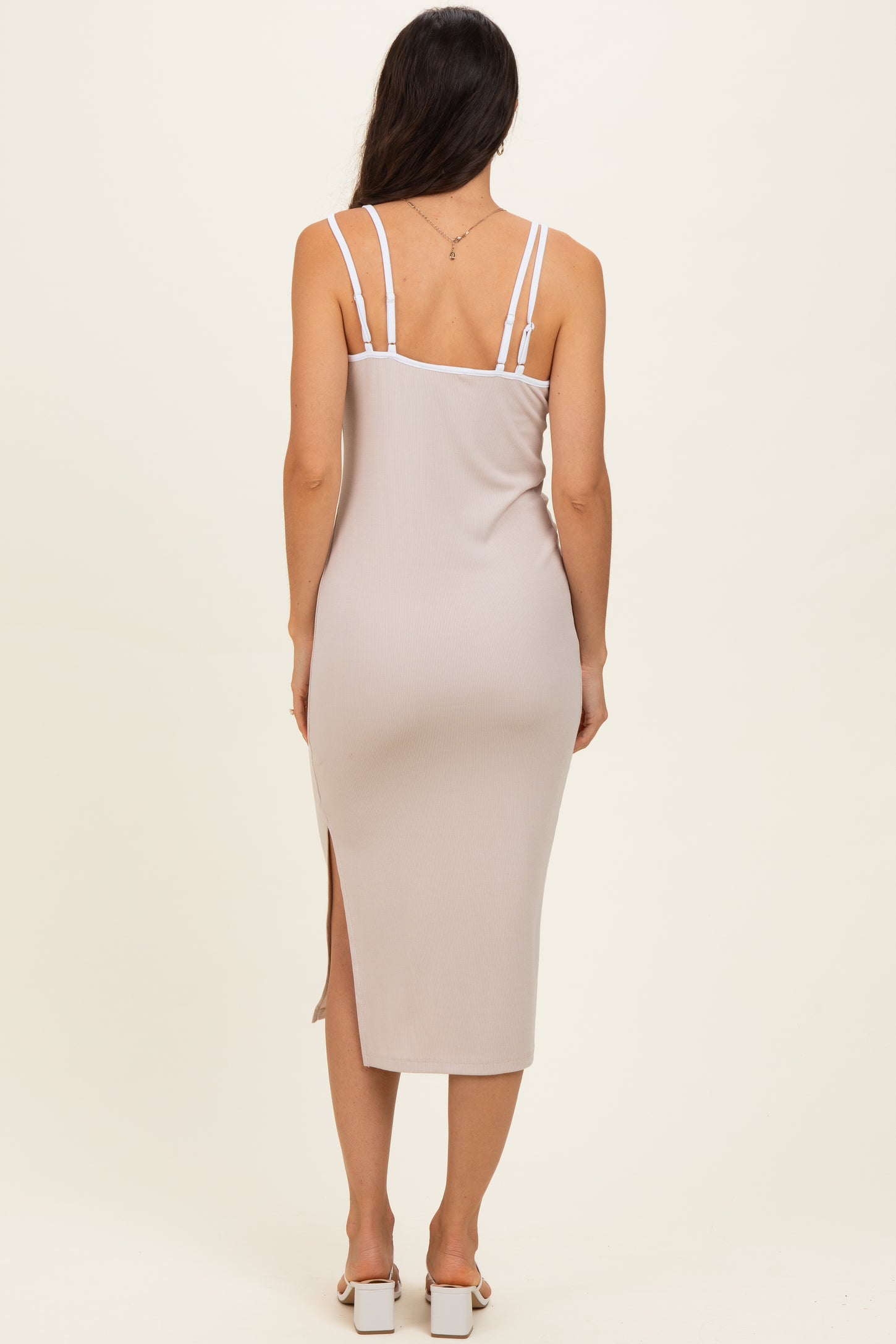 woman wearing a light beige midi dress with adjustable straps and a side slit, viewed from the back