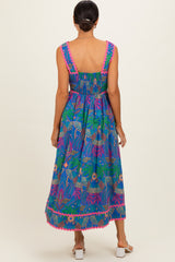 woman wearing a vibrant blue maxi dress with multicolored floral patterns and detailed pink trim at the hem and sleeves