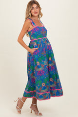 woman wearing a vibrant blue maternity dress with floral patterns and pockets, showcasing her baby bump
