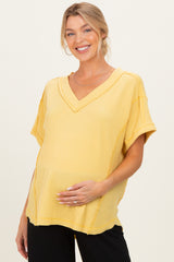 woman wearing a yellow v-neck maternity top with short sleeves and a visible baby bump