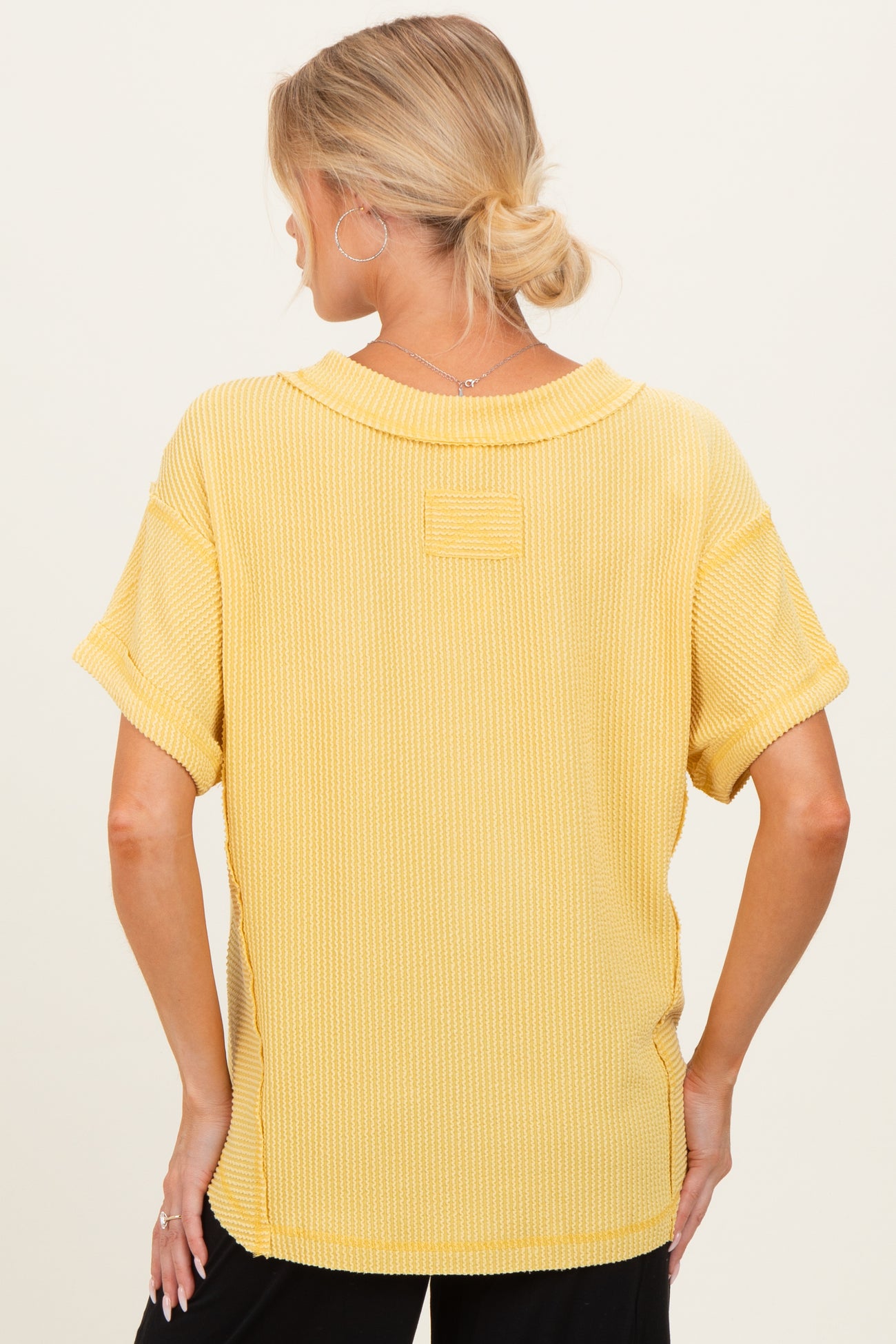 woman wearing a yellow short sleeve maternity top with a relaxed fit and textured fabric, seen from the back