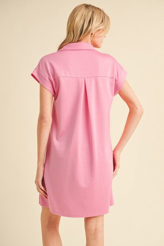 woman wearing a light pink short sleeve shirt dress with a collar and back pleat detail